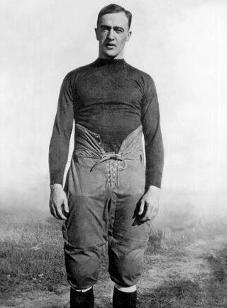 A man in an old football uniform stands on the field.